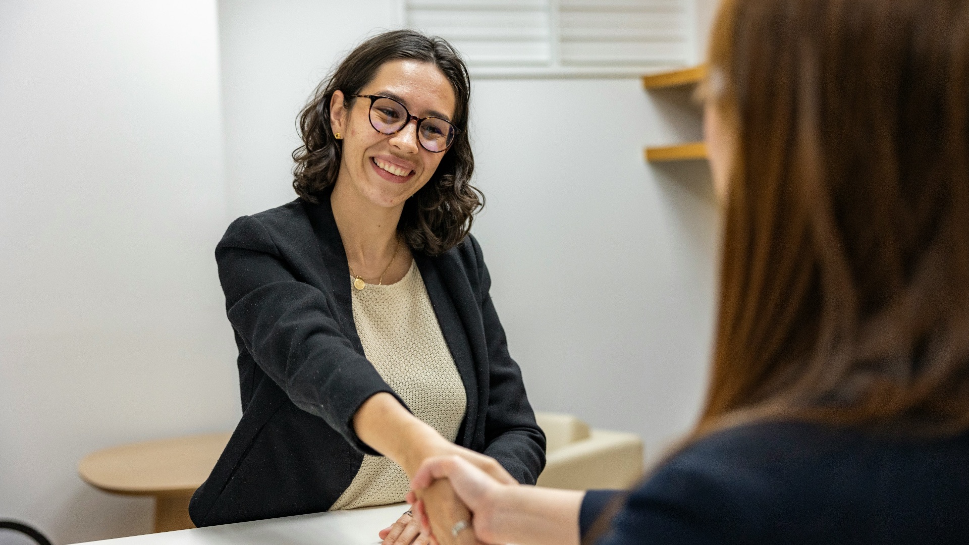 a woman shaking hands with another woman sitting at a table