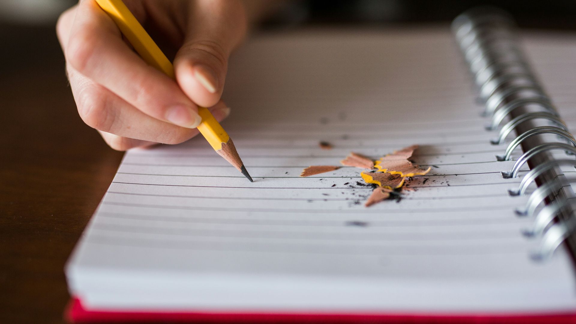 person holding pencil writing on notebook