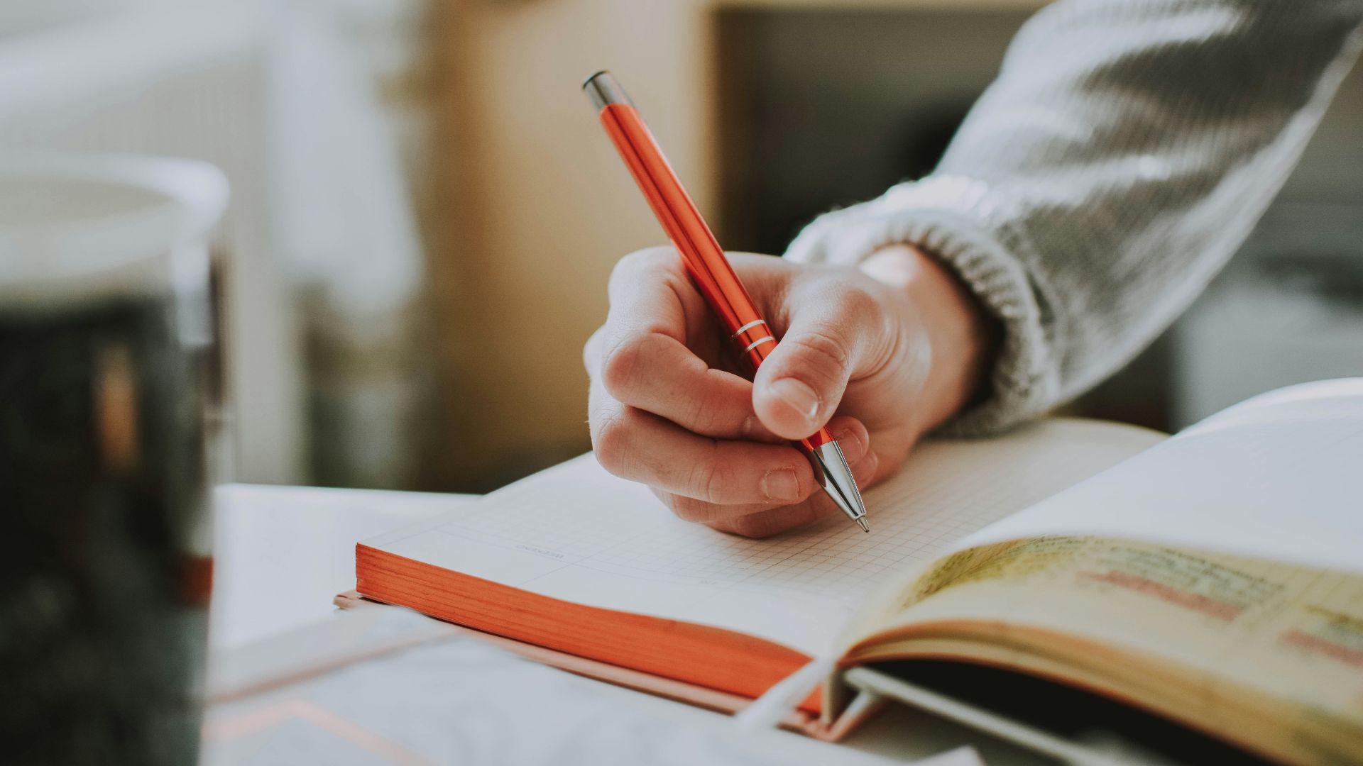 person holding on red pen while writing on book