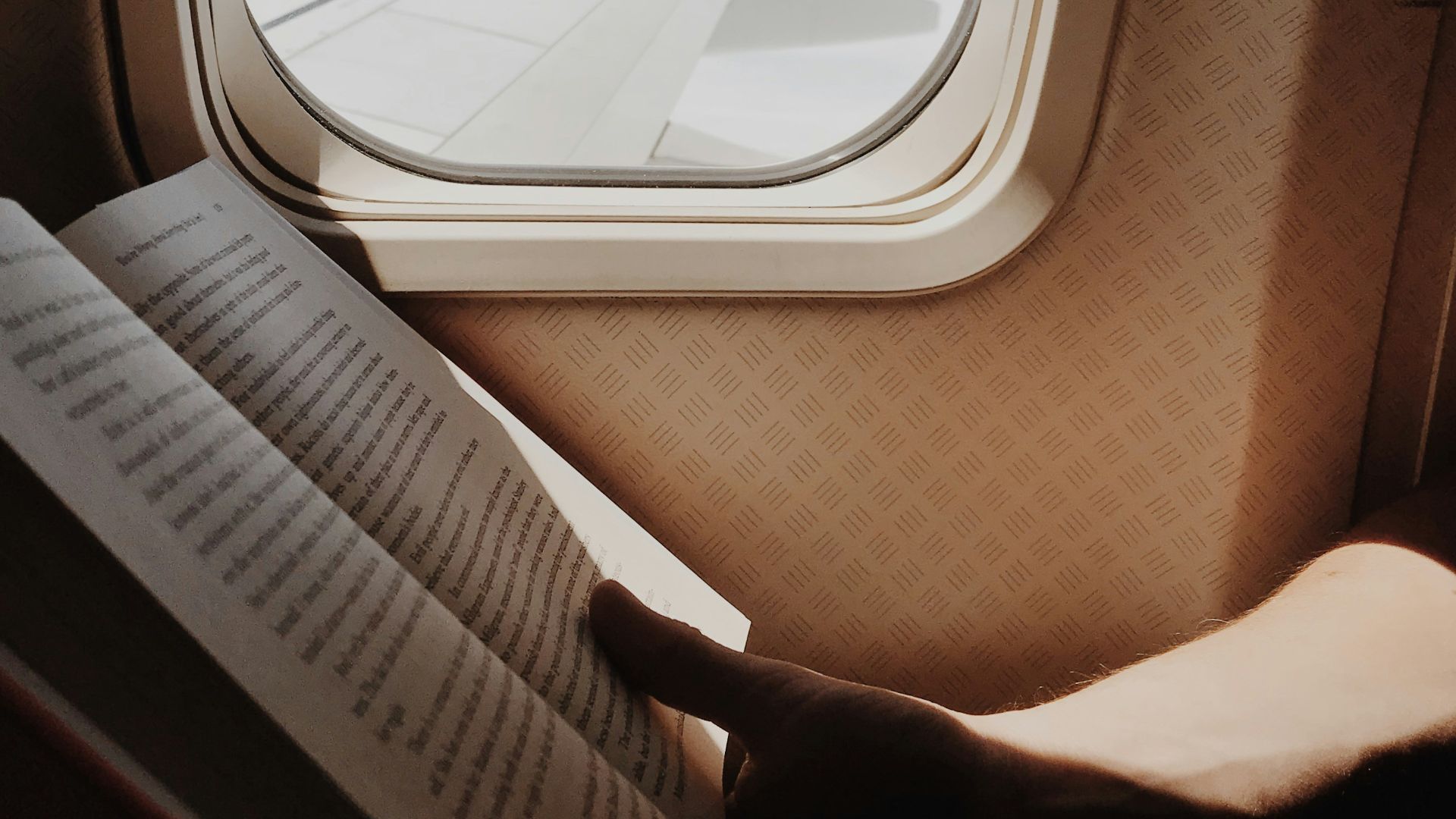 person reading book beside airplane window