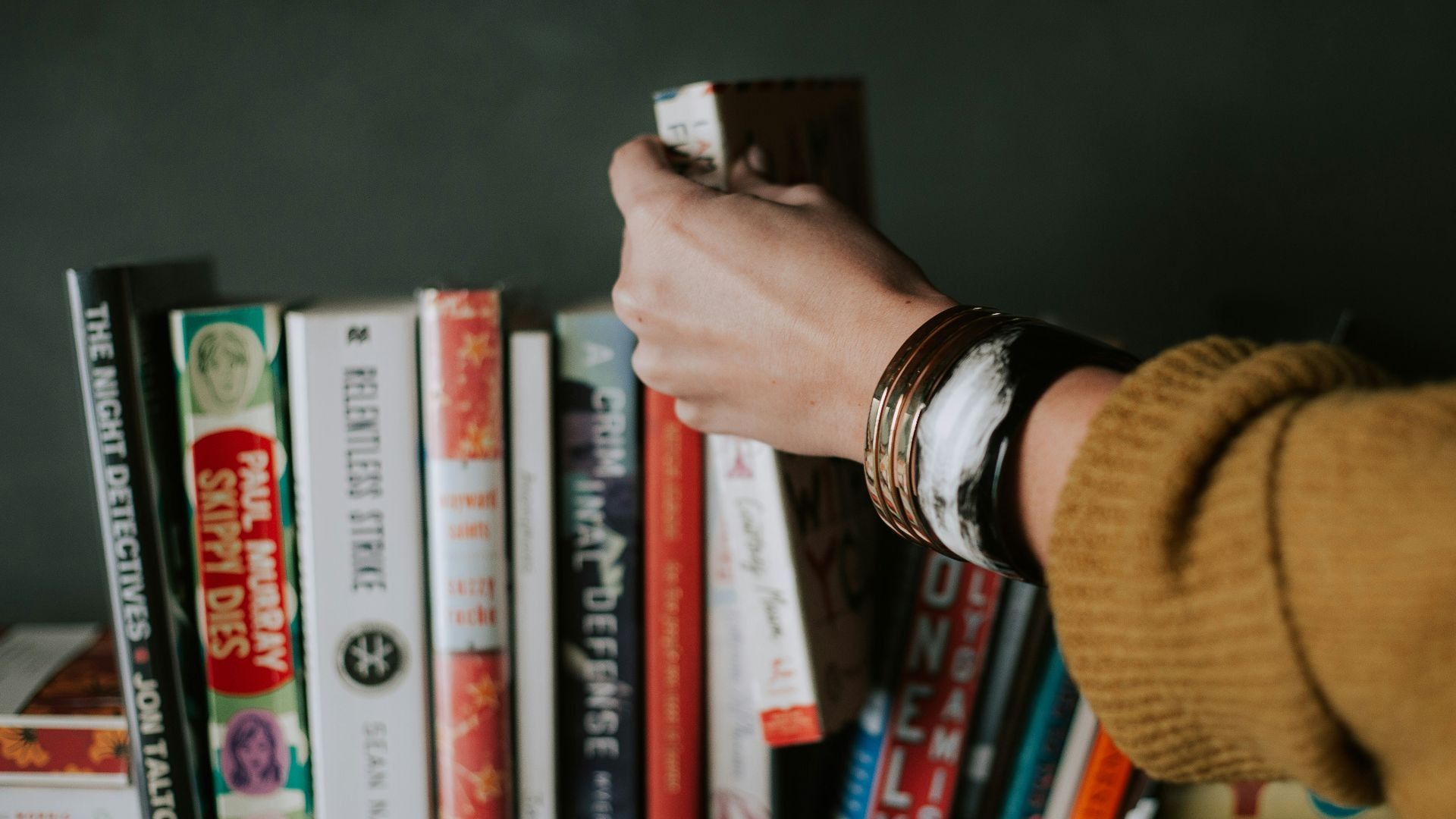 person picking white and red book on bookshelf