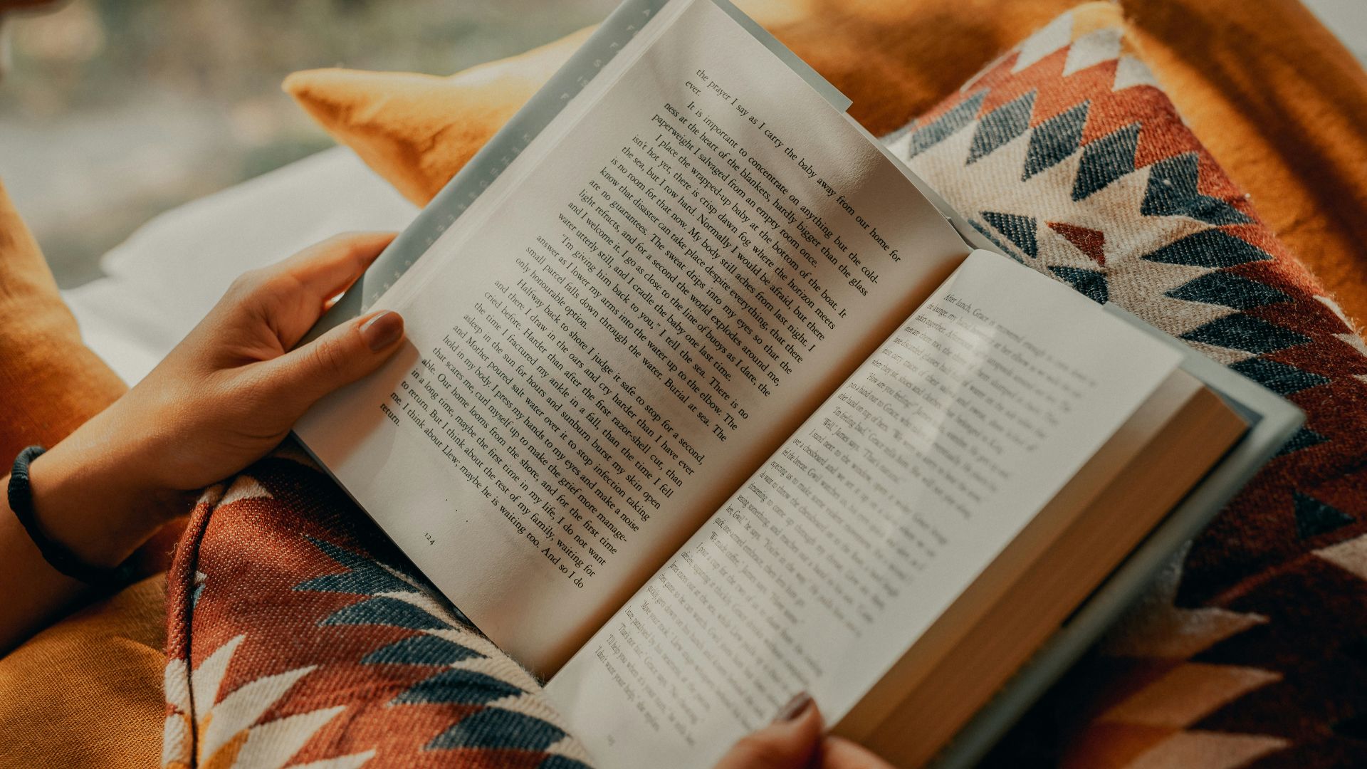 person reading book on brown and beige textile