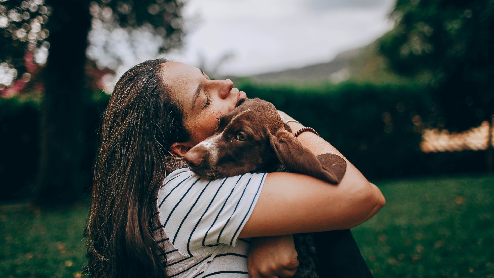 woman in white and black stripe shirt hugging brown short coated dog