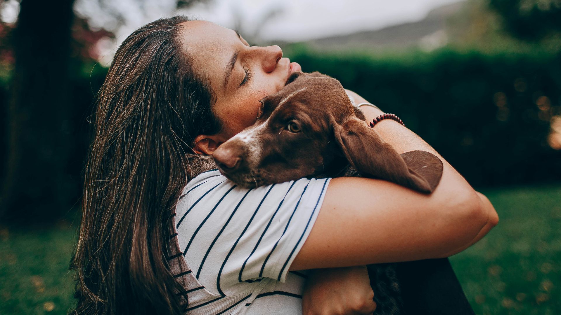 woman in white and black stripe shirt hugging brown short coated dog
