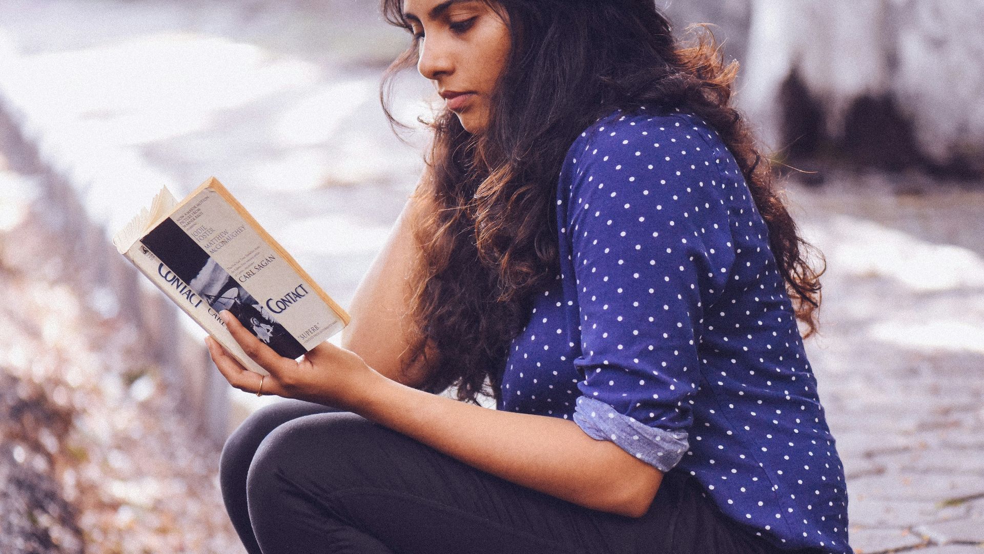 woman sitting on gutter reading book