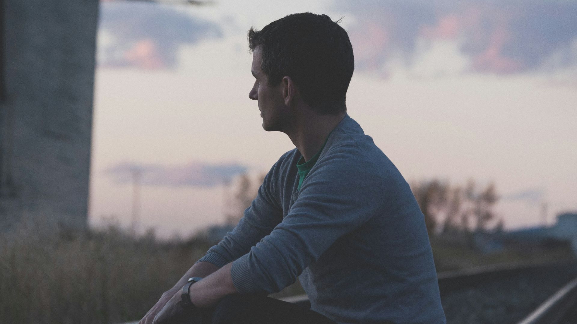 man sitting on railway under gray sky