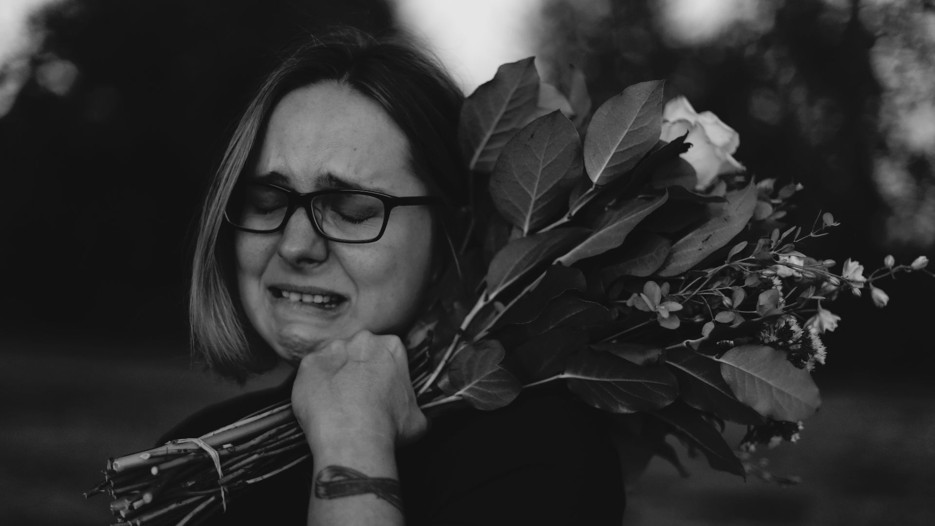 grayscale photo of crying woman holding bouquet of flowers