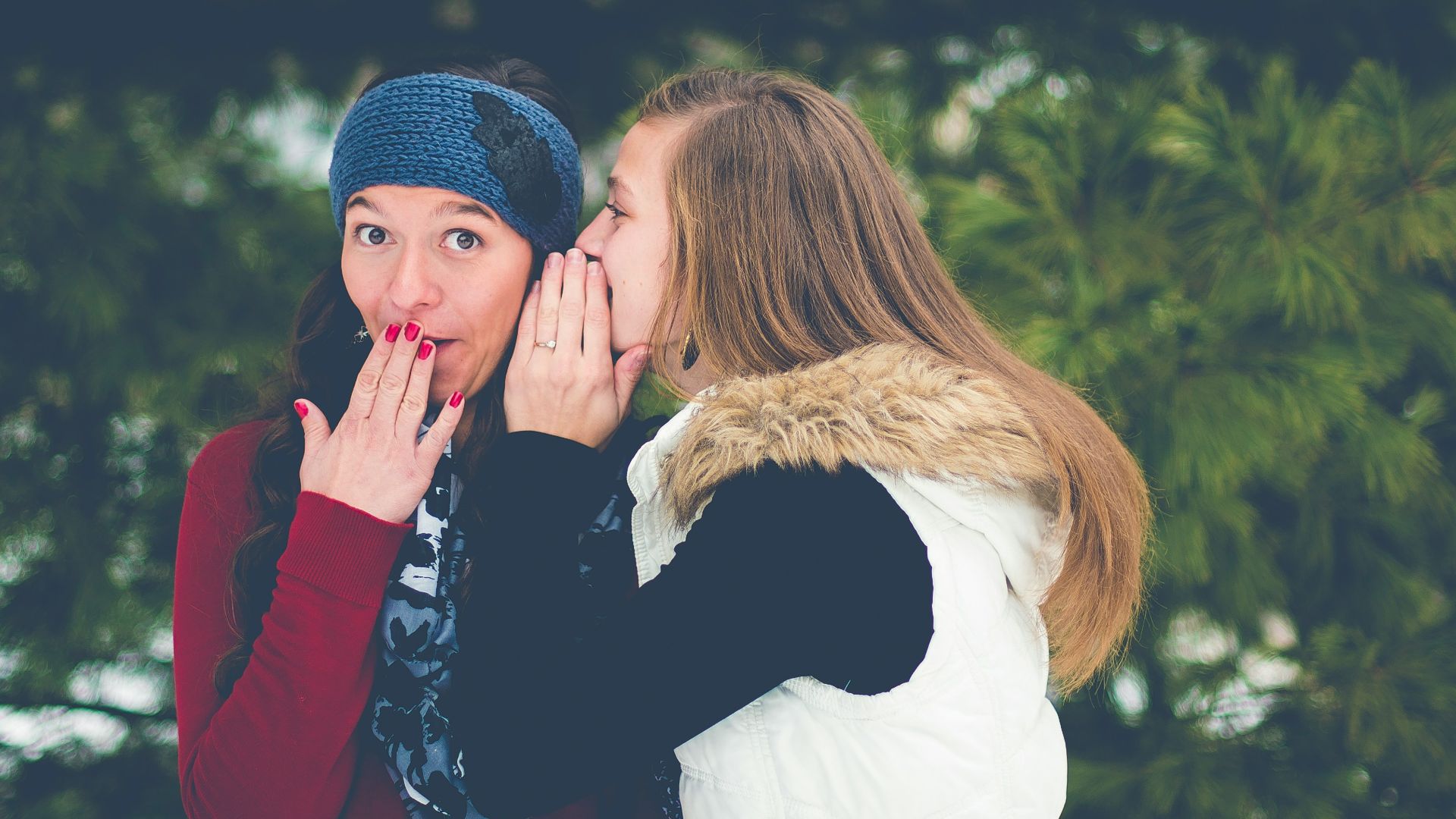 woman whispering on woman's ear while hands on lips