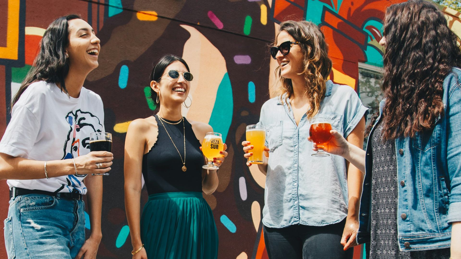 four women holding drinks while laughing together during daytime
