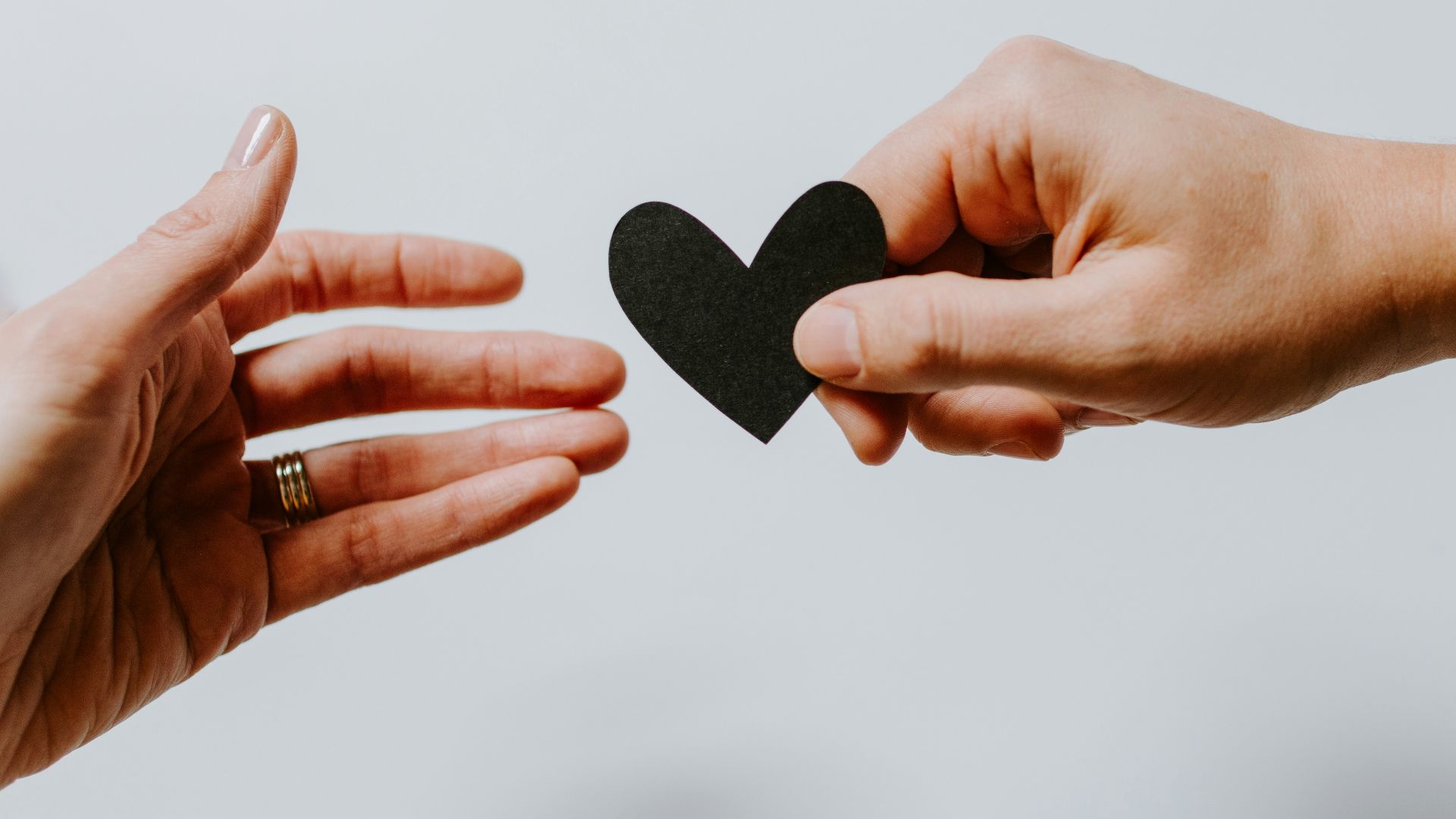 person reaching black heart cutout paper