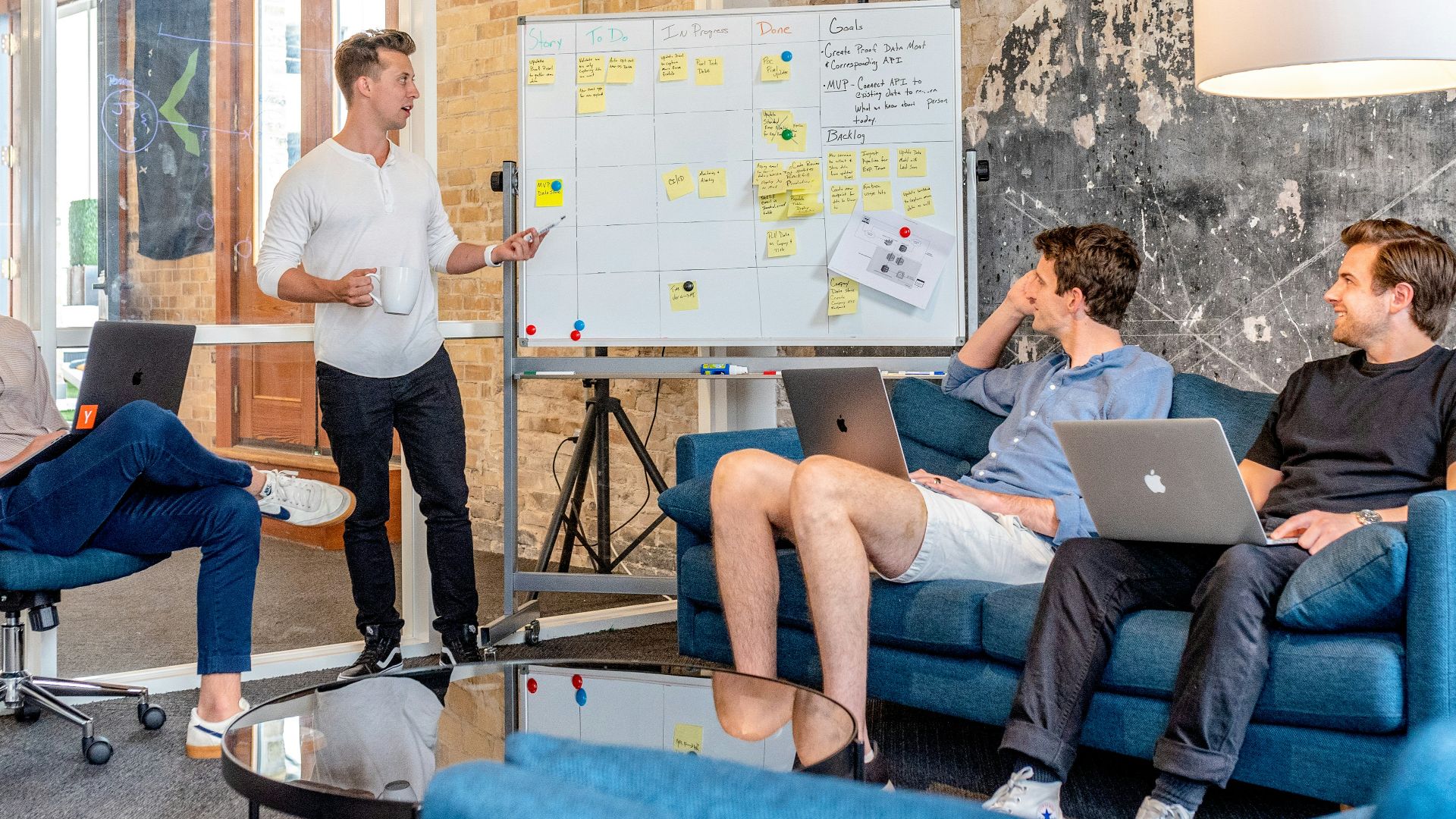 three men sitting while using laptops and watching man beside whiteboard