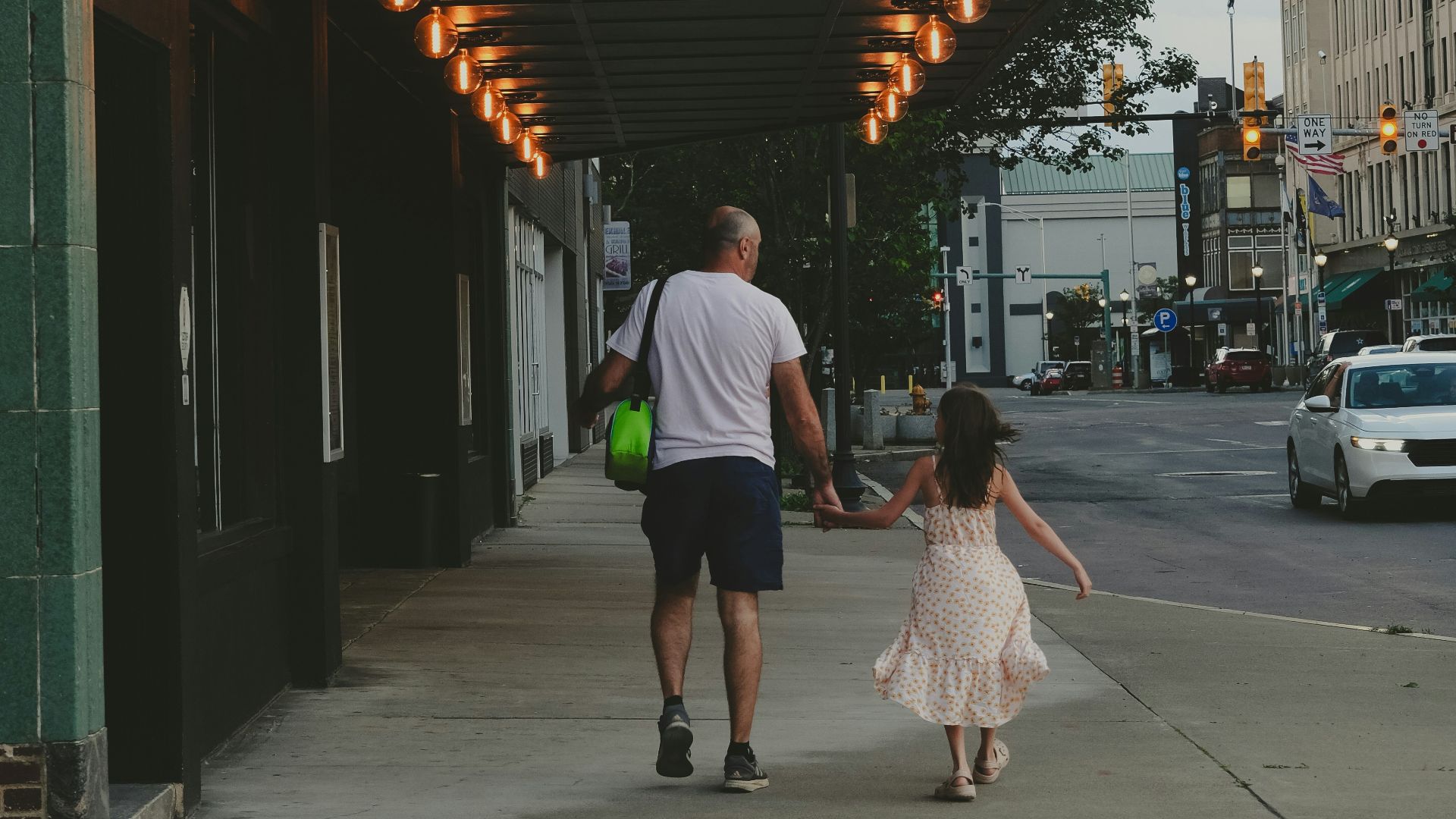 a man and a little girl walking down a sidewalk