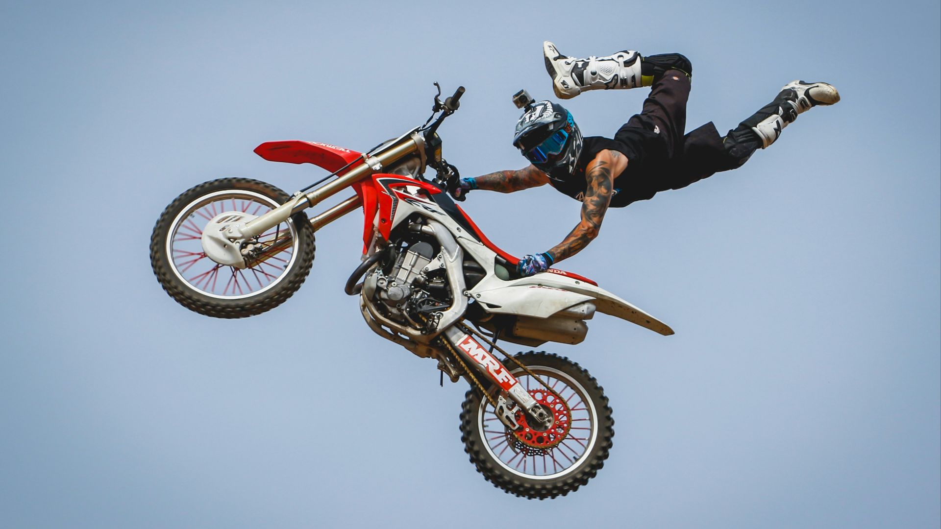 male rider with arm tattoos riding dirt bike doing trick on mid air during daytime