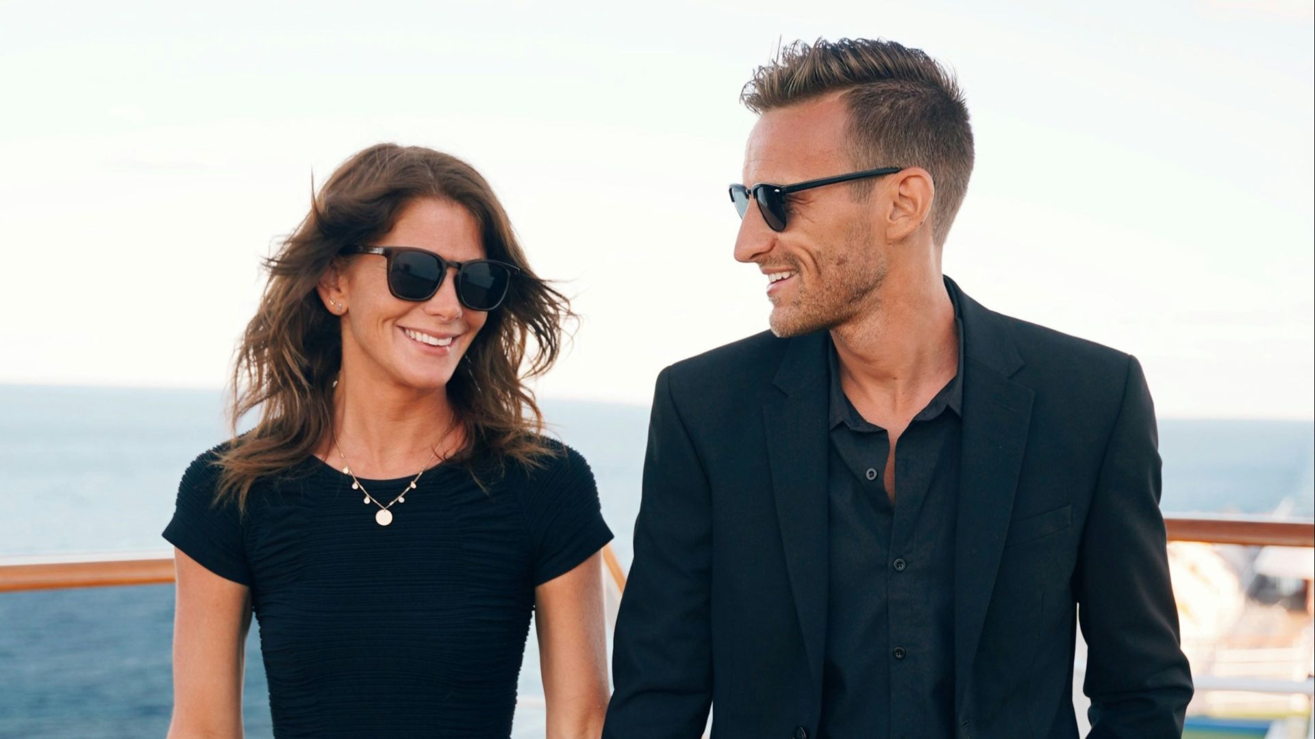 a man and woman wearing sunglasses and standing on a deck