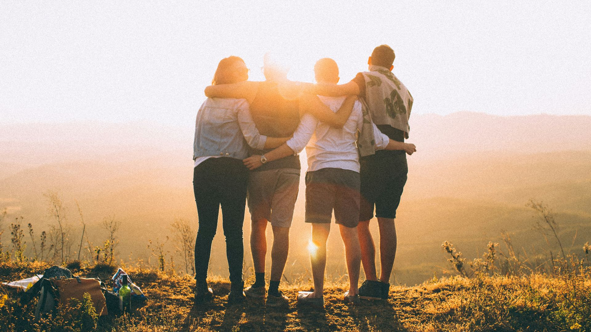four person hands wrap around shoulders while looking at sunset