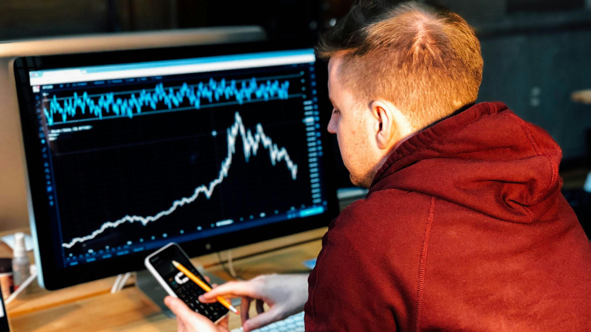 man holding black smartphone with flat screen monitor in front