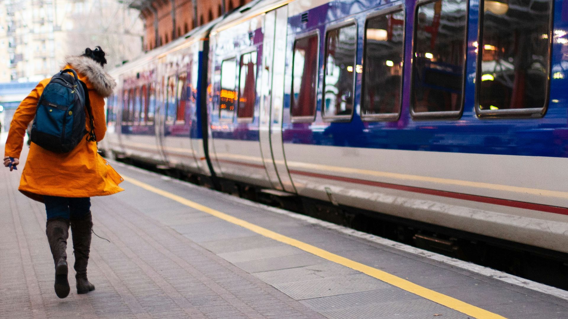 woman in orange coat walking beside train at the station