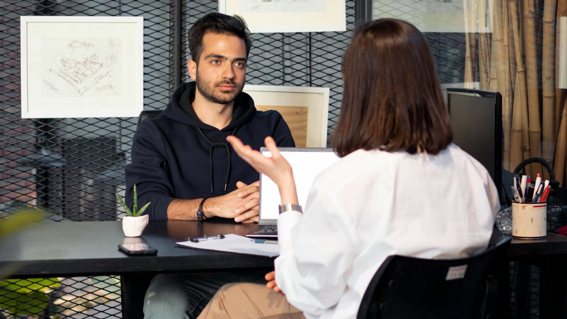 a man sitting at a desk talking to a woman