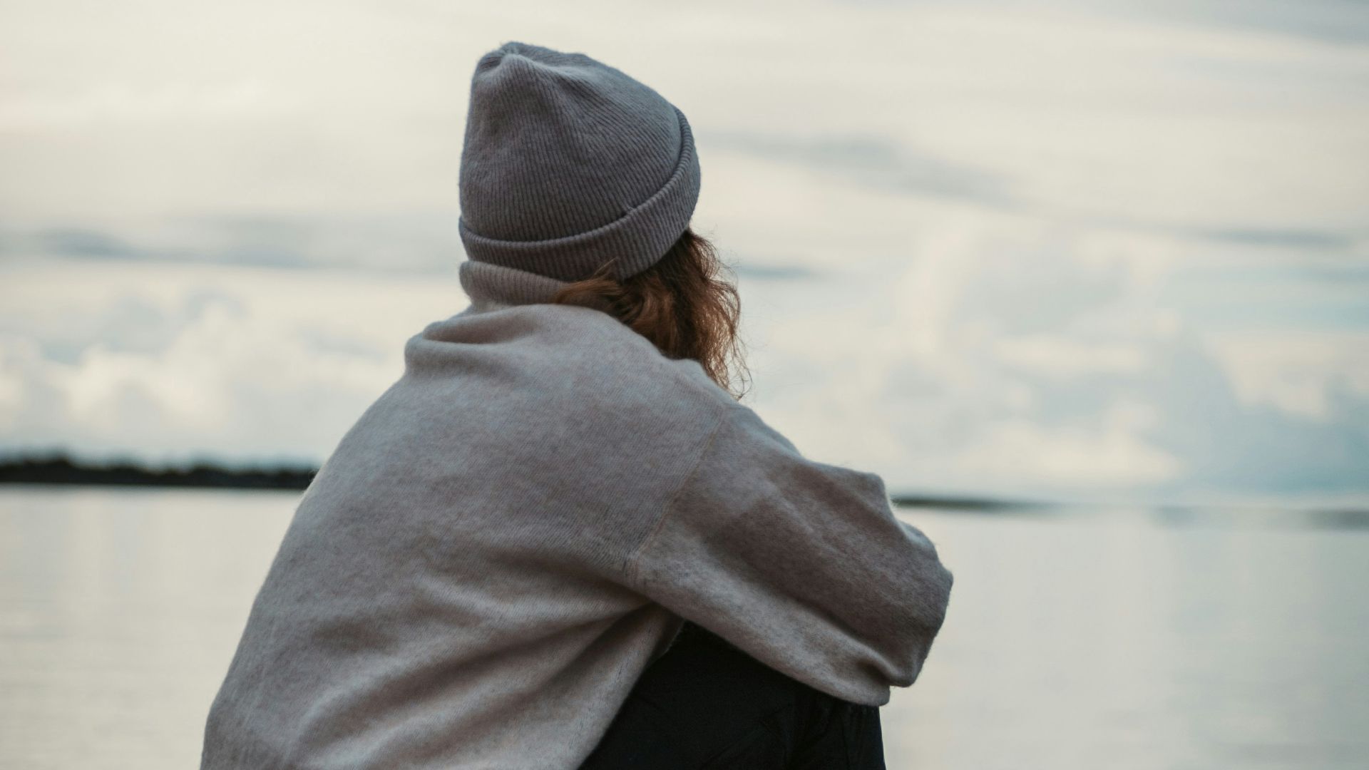 person in gray hoodie and black pants sitting on brown wooden dock during daytime