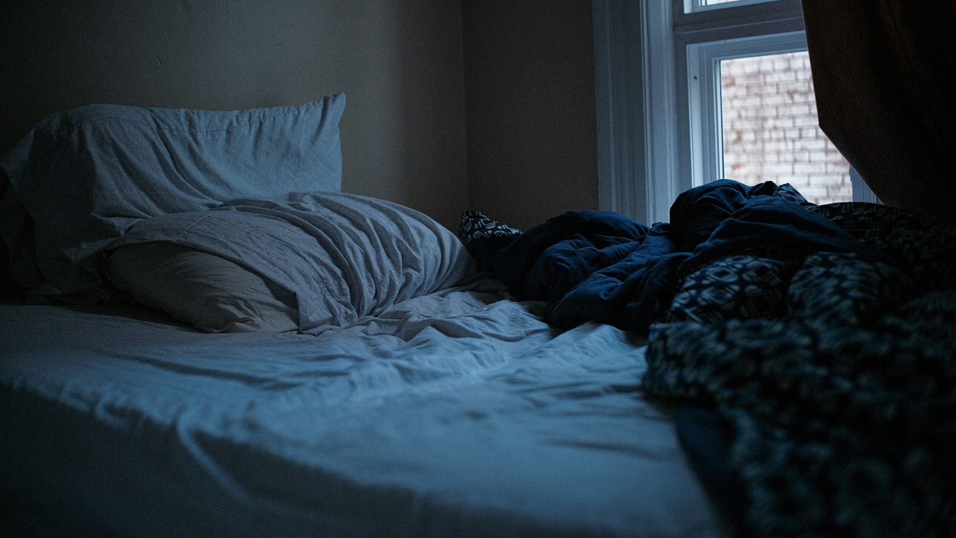An unmade bed in a dark, quiet bedroom.