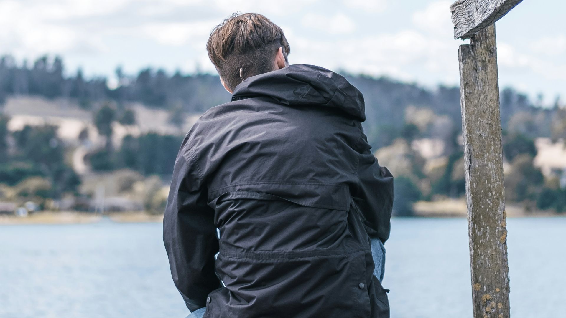 man in black jacket sitting on wooden dock during daytime