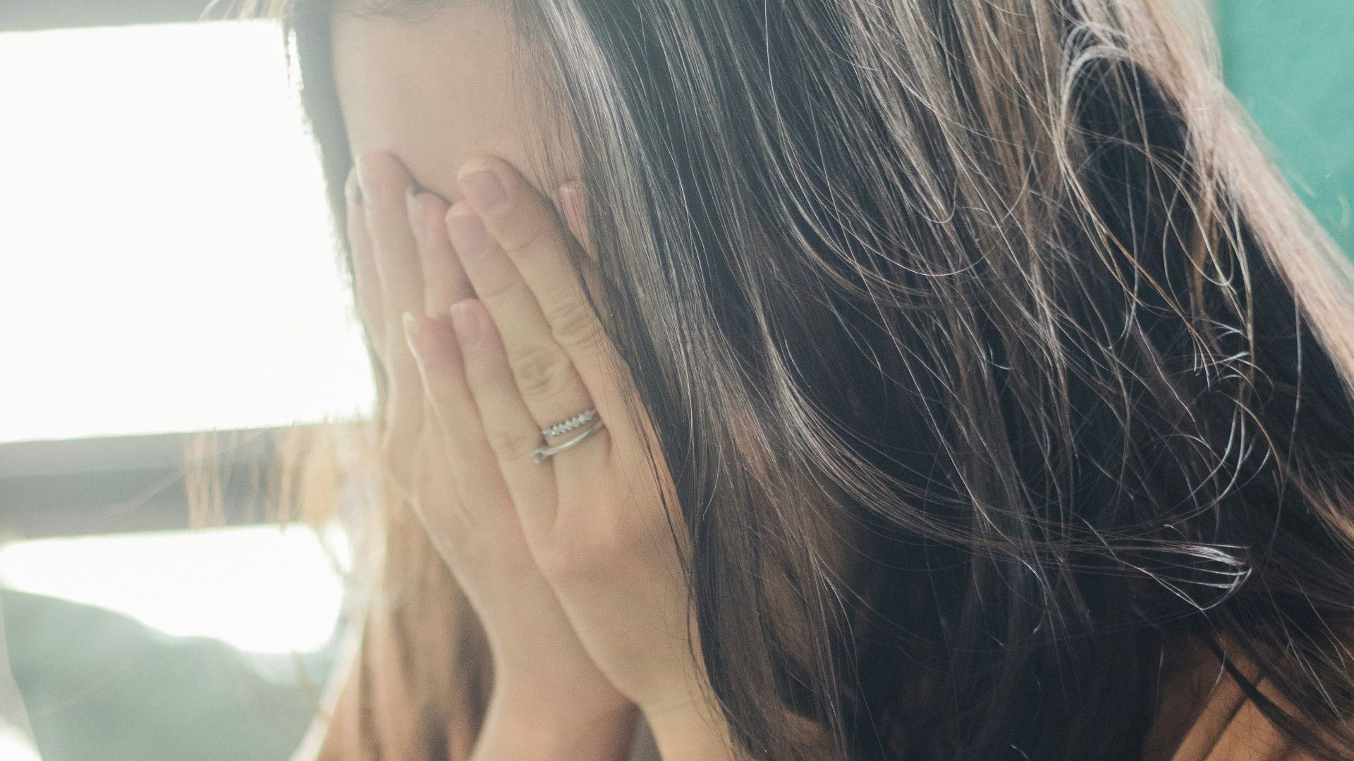 woman in brown shirt covering her face