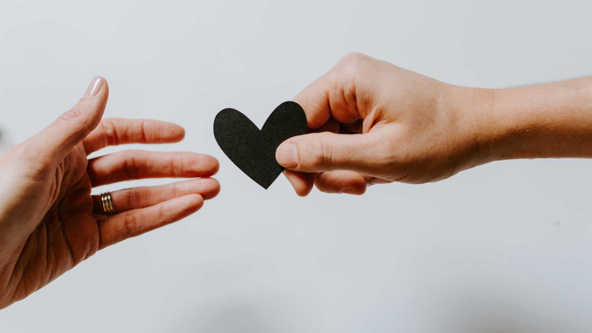 person reaching black heart cutout paper