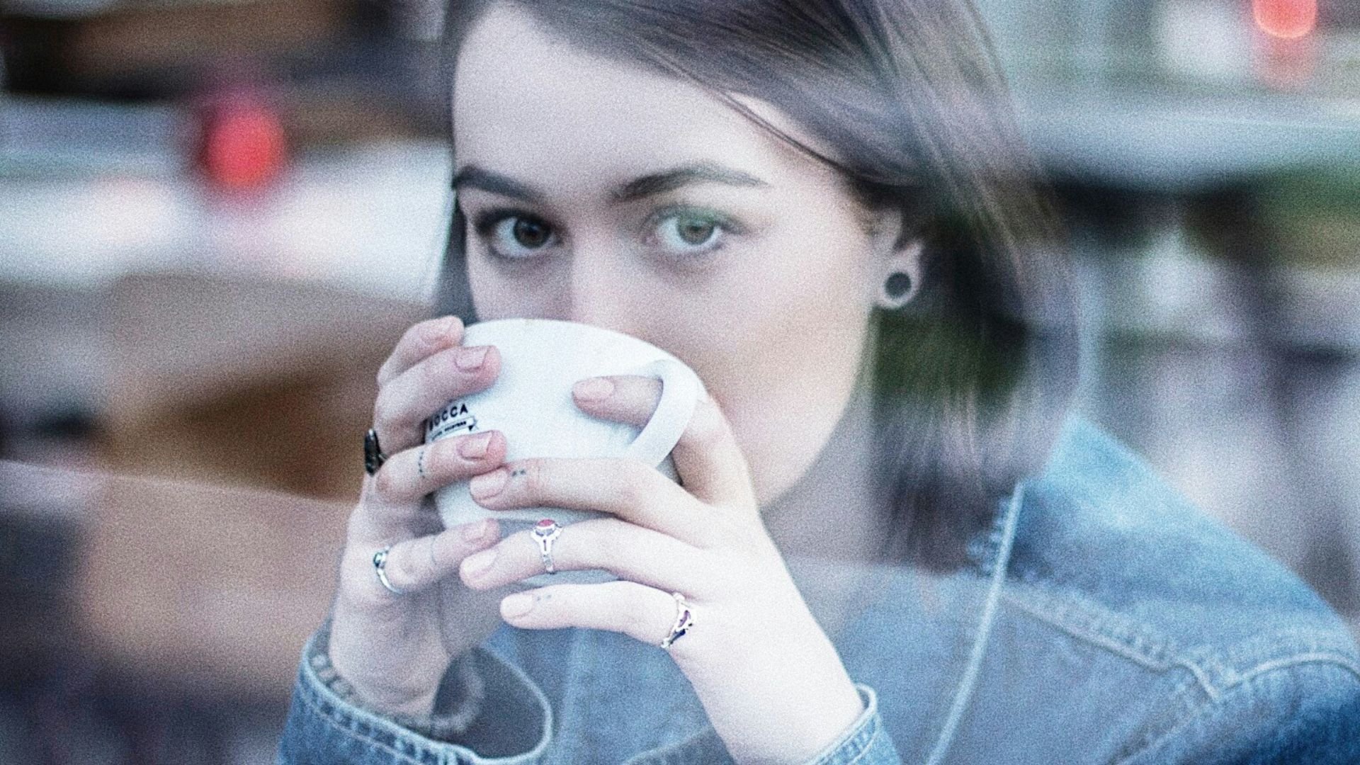 woman wearing blue denim jacket holding white ceramic teacup