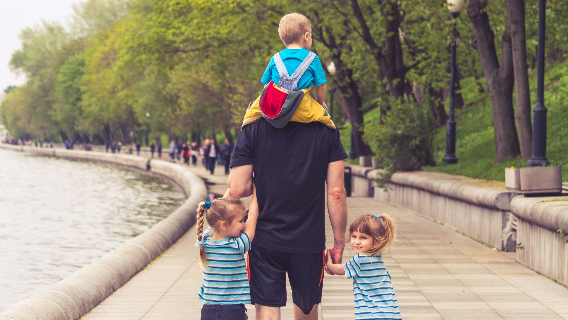 man in black t-shirt and brown shorts holding girl in blue and black jacket walking