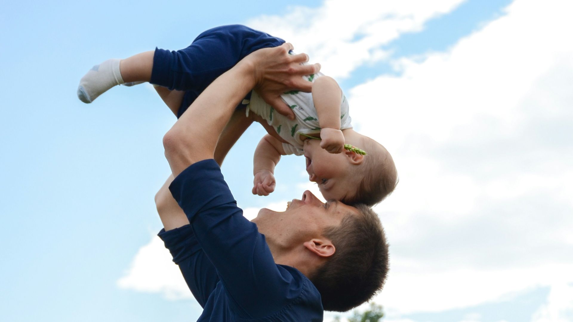 man in blue long sleeve shirt carrying baby in white onesie