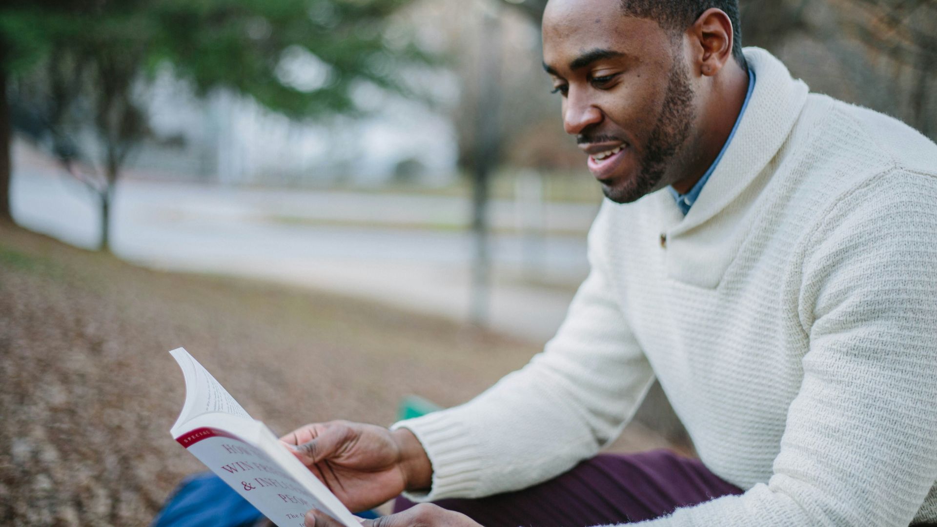 man wearing white sweater while reading book