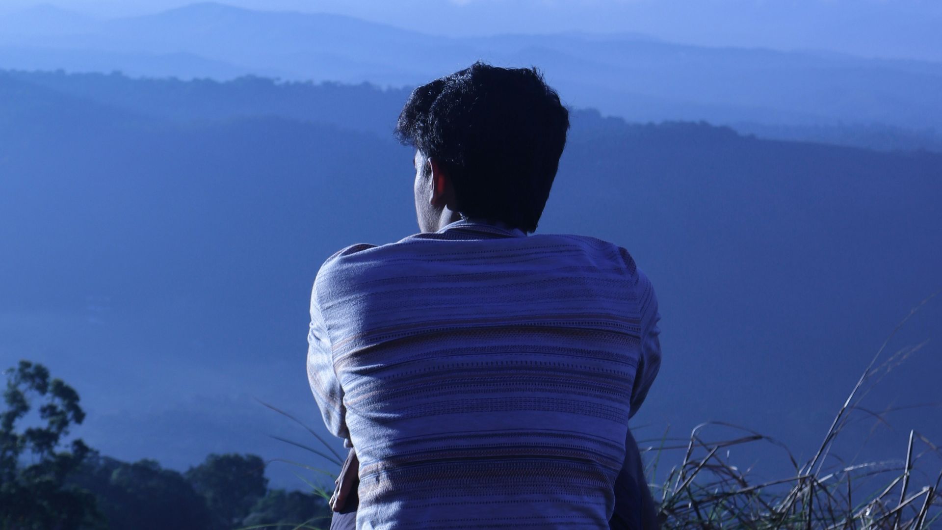 man in white shirt sitting on rock looking at mountains during daytime