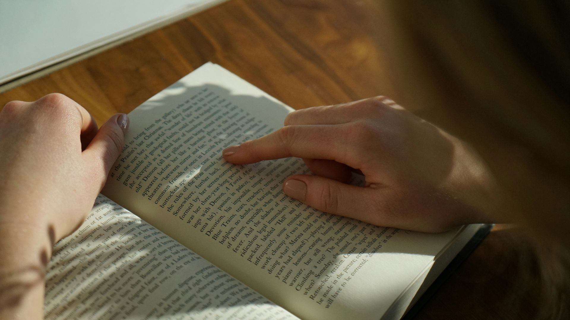 person reading book on brown wooden table taken at daytome