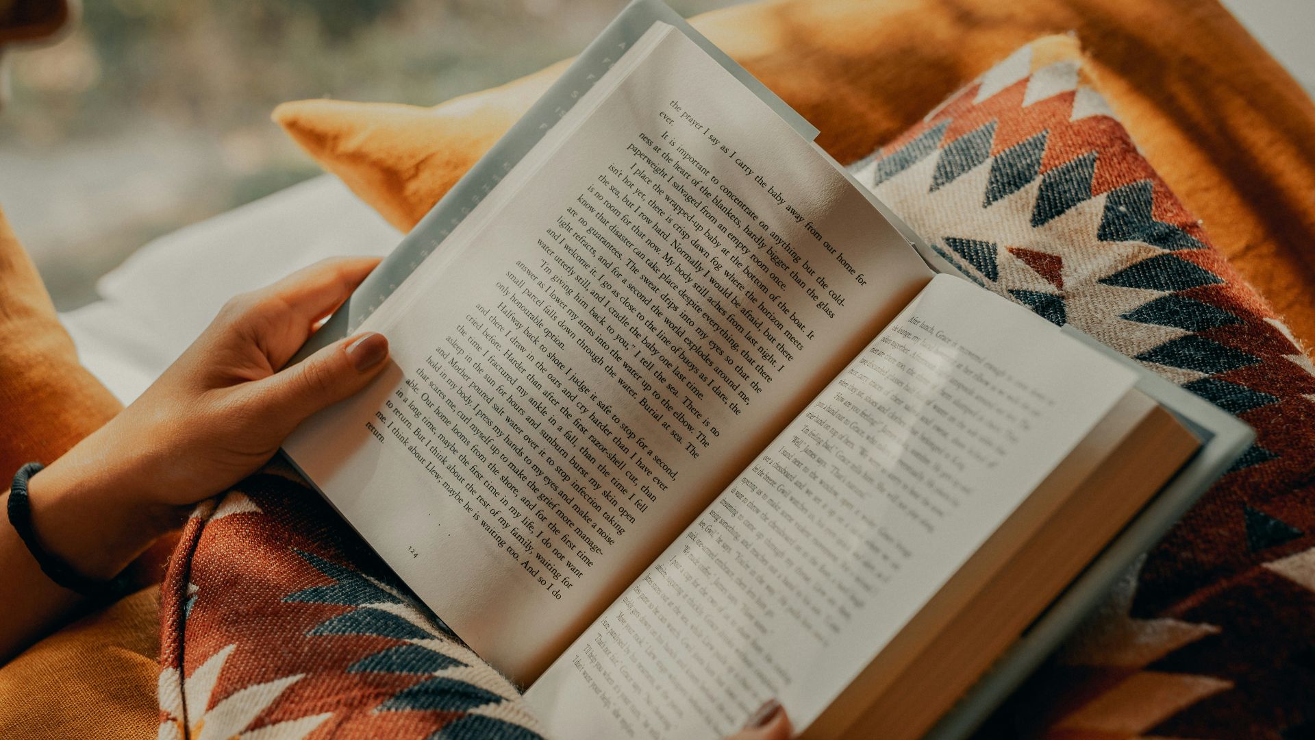 person reading book on brown and beige textile