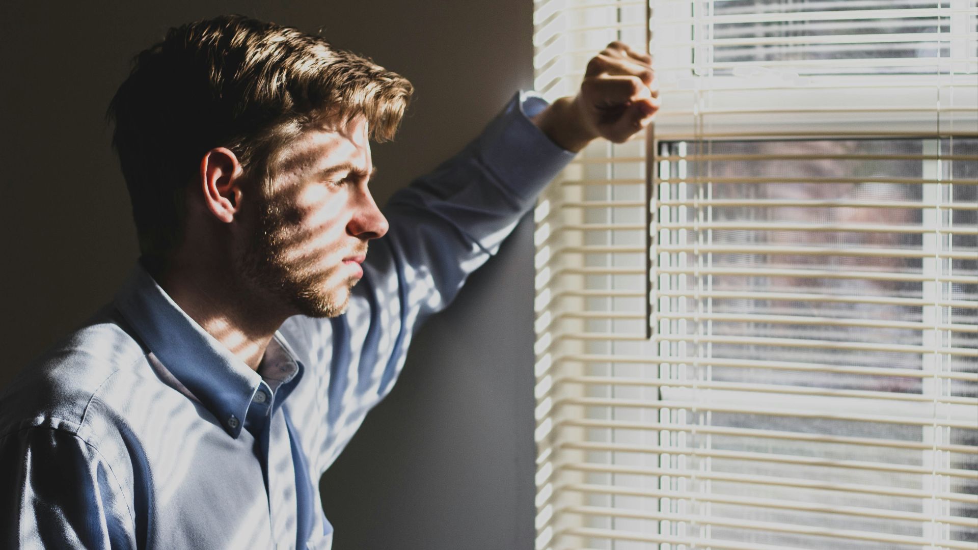 person near clear glass window pane and window blinds low-light photography