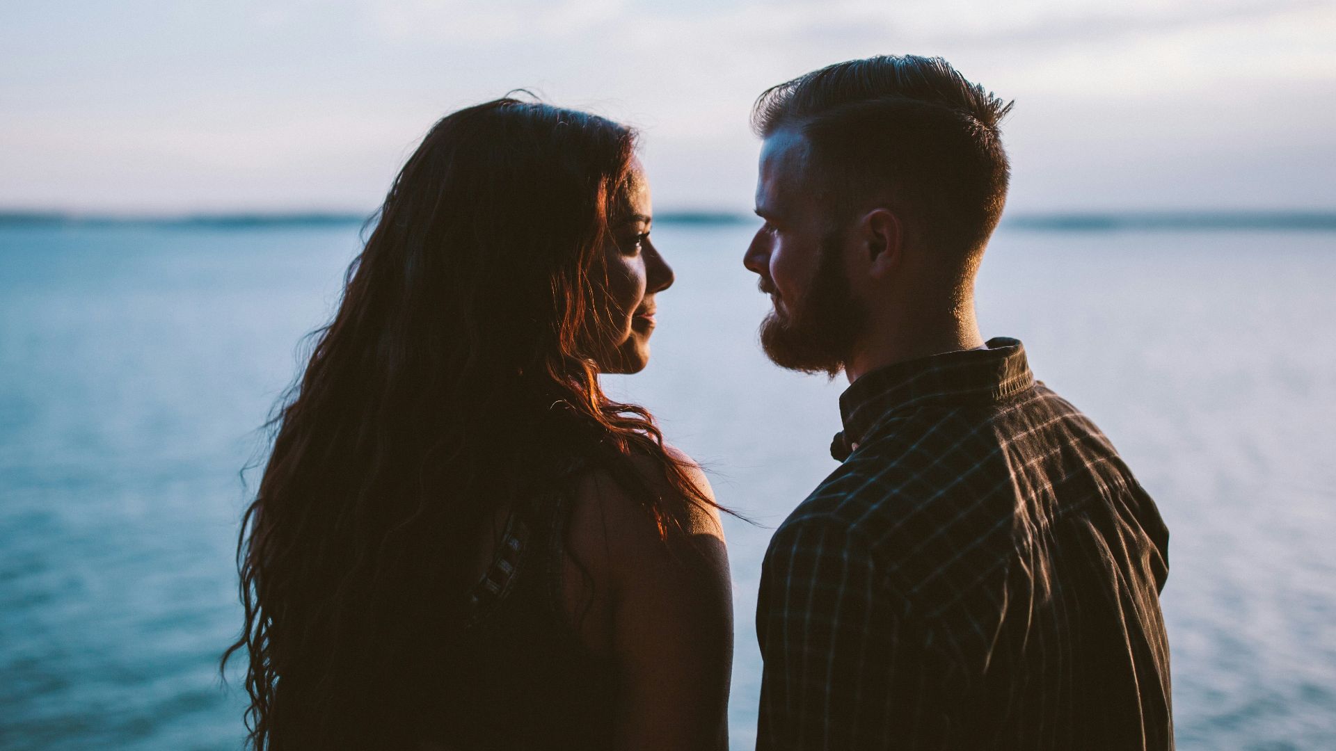man and woman standing while looking each other near body of water