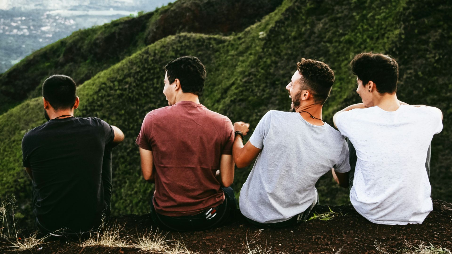 row of four men sitting on mountain trail