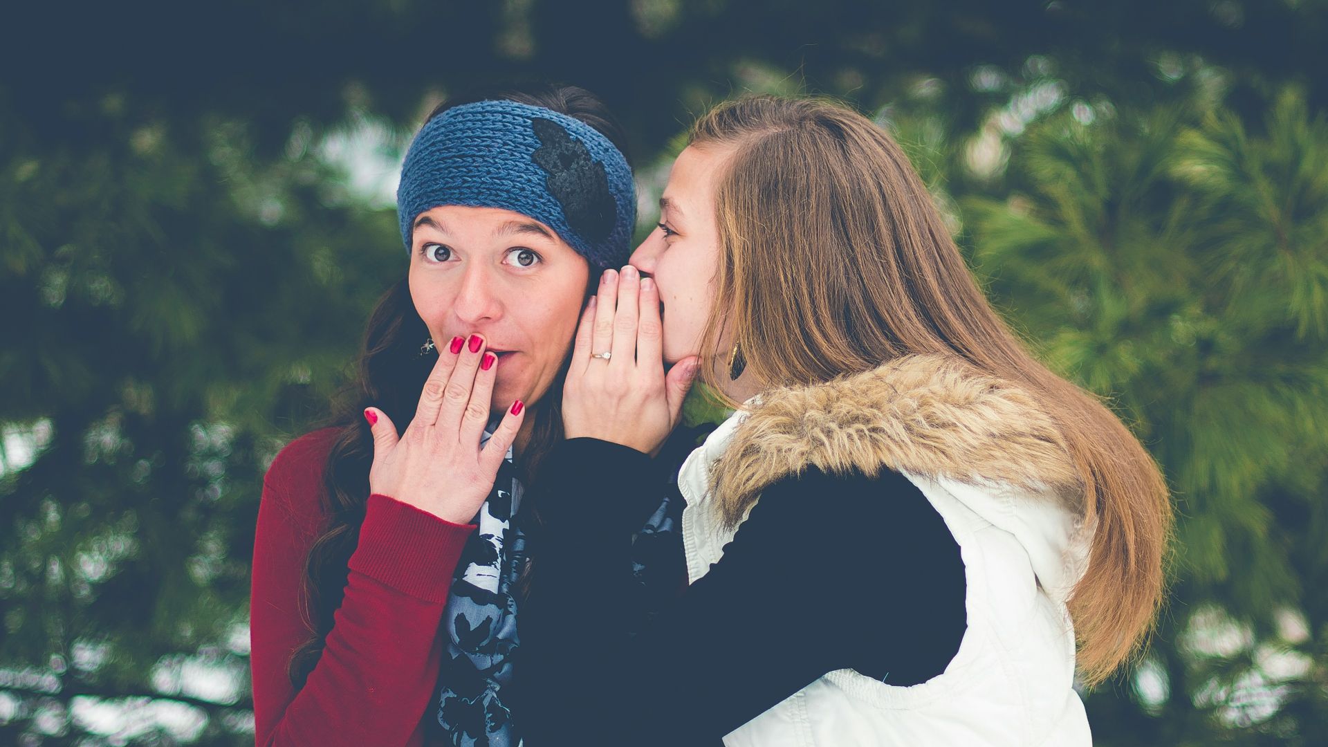 woman whispering on woman's ear while hands on lips
