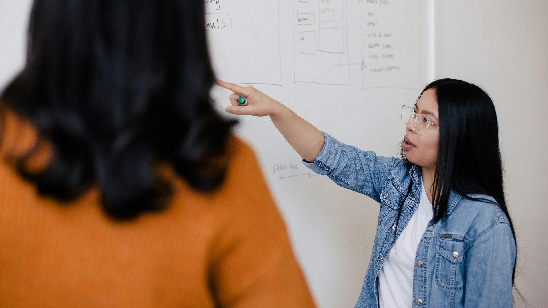 two women standing in front of white dry erase board