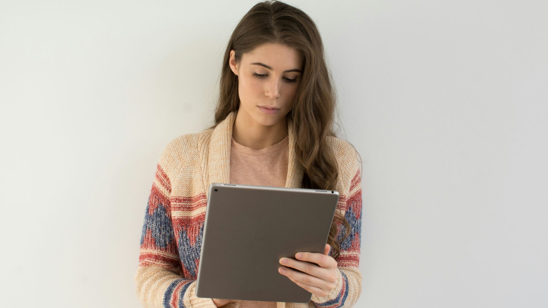 woman in beige, gray, and red sweater holding silver tablet computer