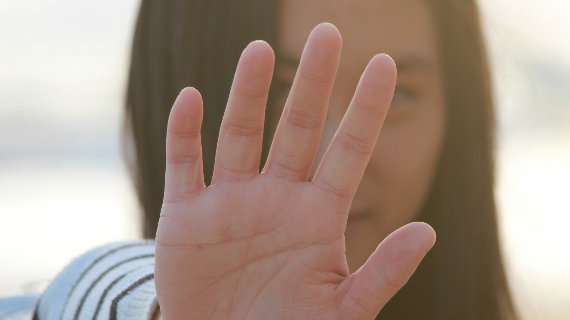 woman in white and gray striped long sleeve shirt covering her face with her hand