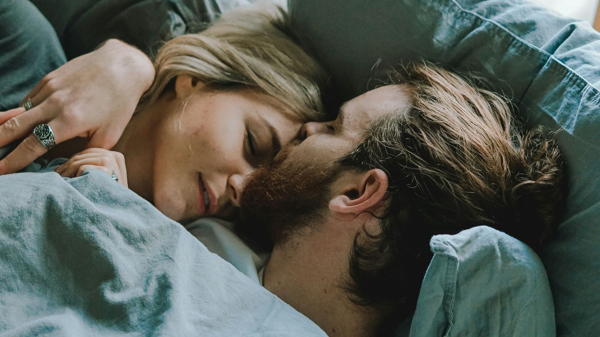 man kissing woman's forehead while lying on bed
