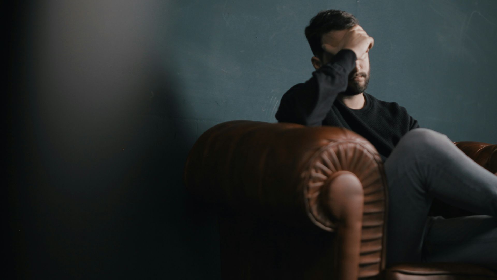 a man holds his head while sitting on a sofa