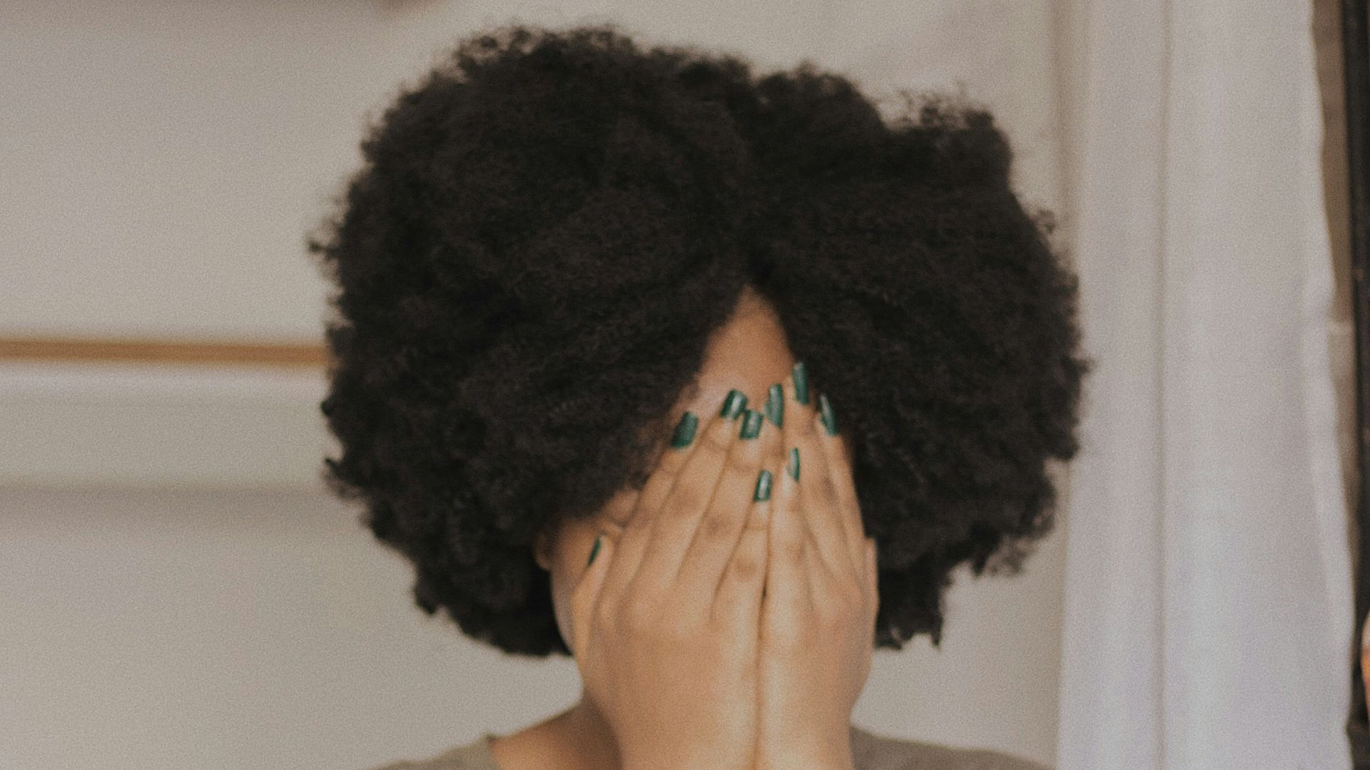 woman in gray t-shirt covering face with both hands