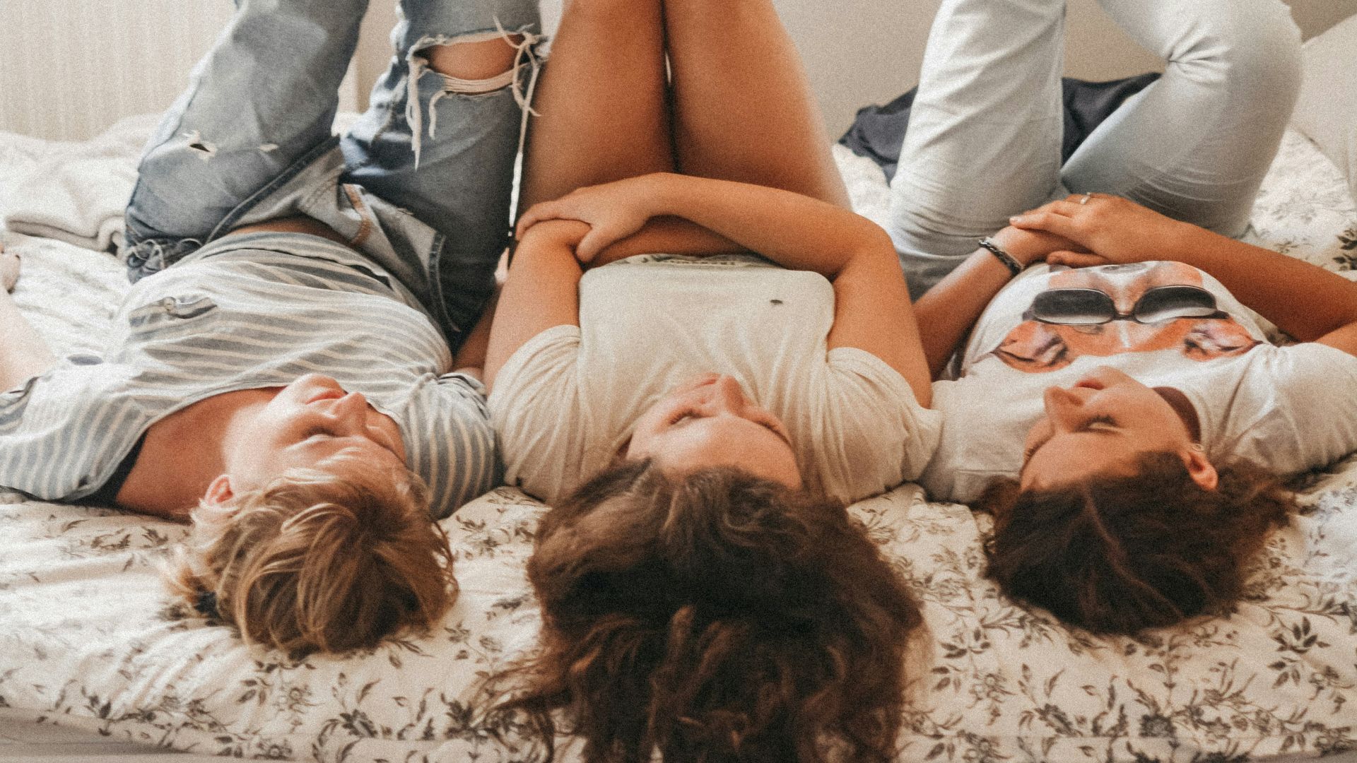 three women lying on bed while raising their feet