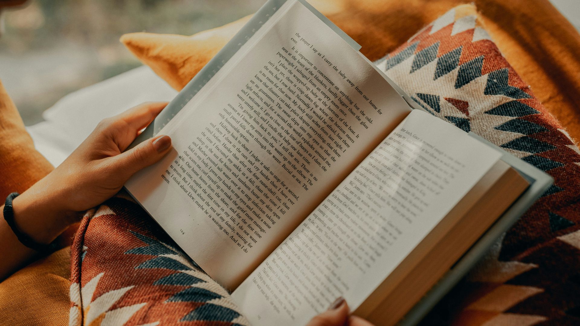 person reading book on brown and beige textile