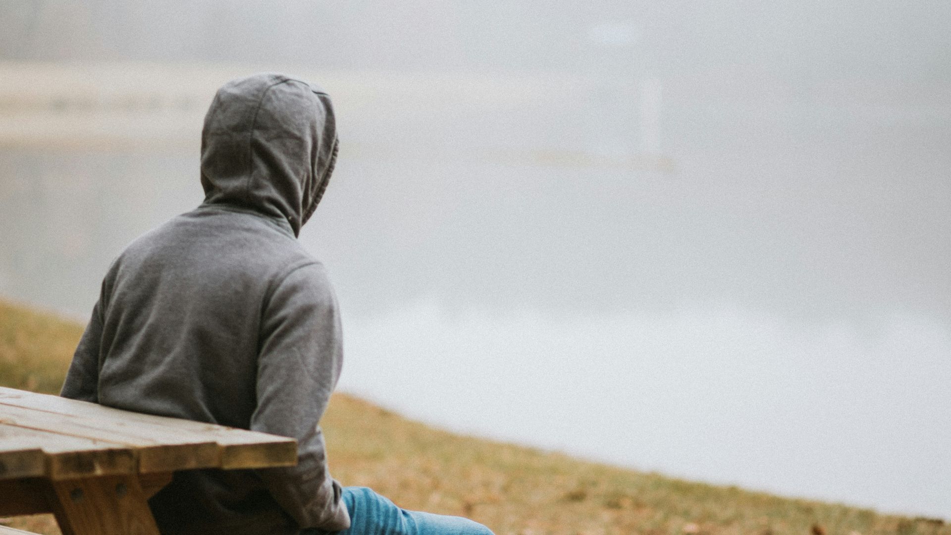 person in gray hoodie sitting on picnic table staring at the fog during daytime