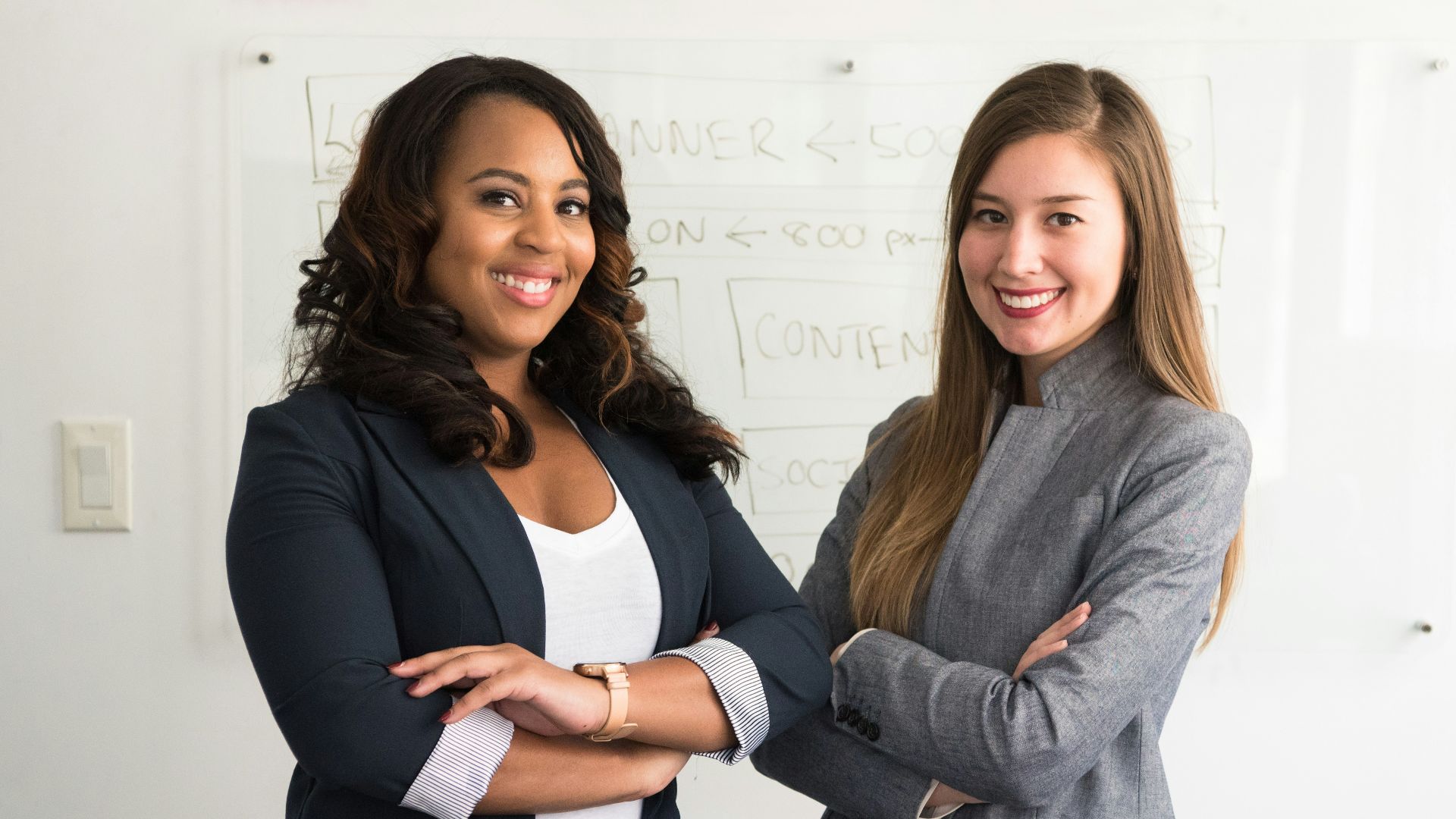 two women in suits standing beside wall