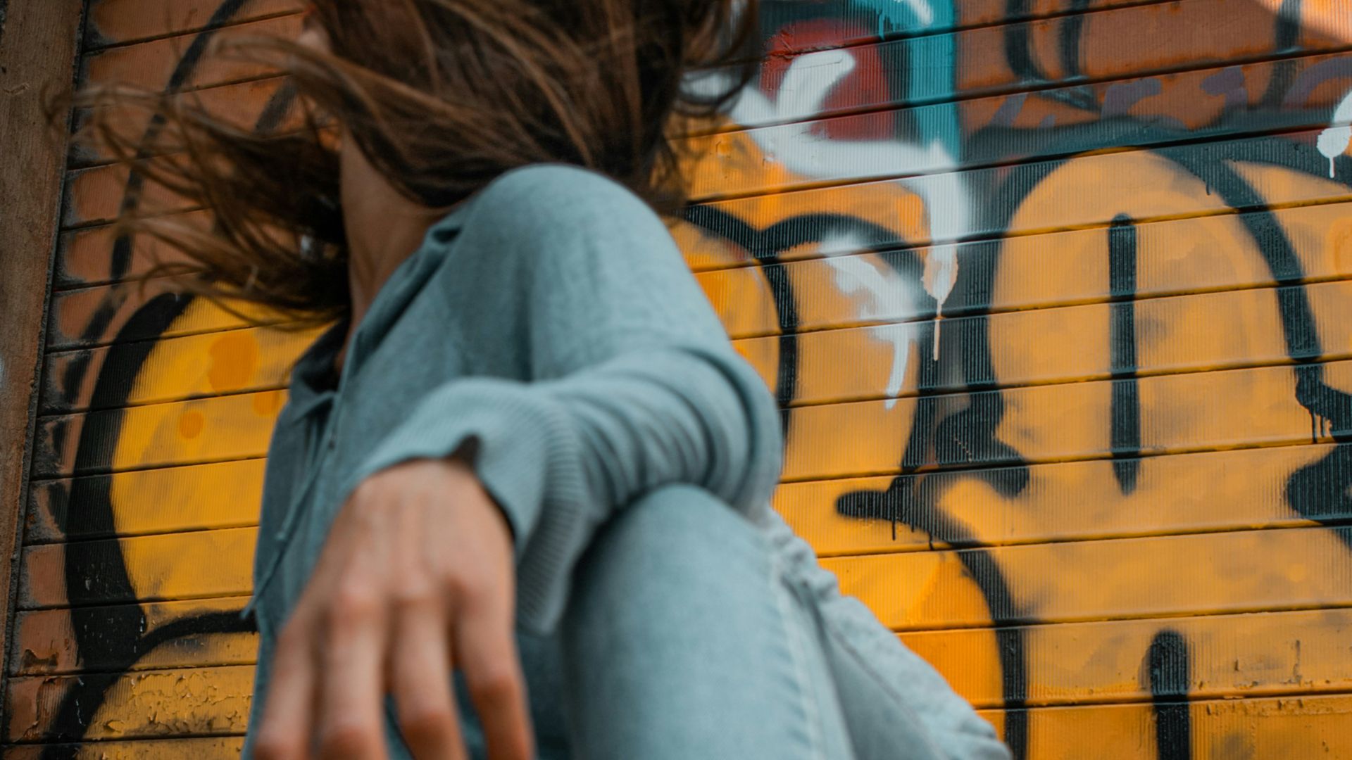 woman in gray hoodie and blue denim jeans sitting on brown wooden bench