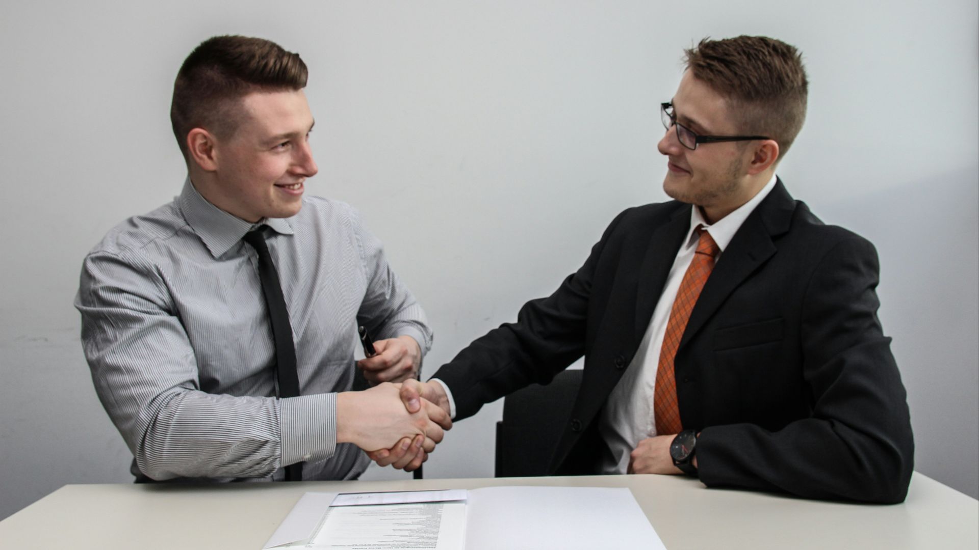two men facing each other while shake hands and smiling